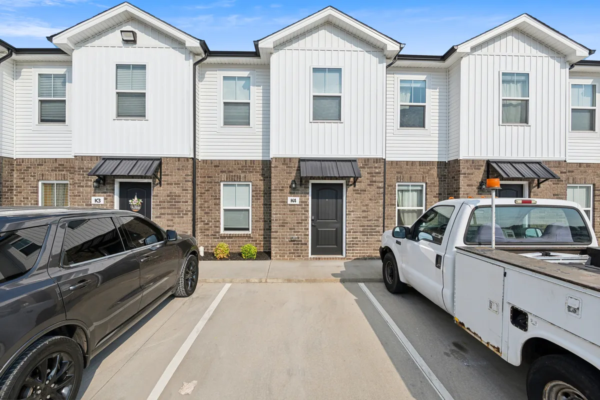 This exterior image highlights the front doors of the townhouses with vehicles parked conveniently in front. Well-maintained landscaping with flowers adds a welcoming touch, emphasizing the accessible parking feature.