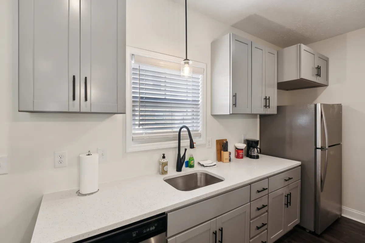A cozy kitchen scene featuring modern cabinetry, stainless steel appliances, a countertop sink, and a window with blinds letting in natural sunlight. The setup is functional yet warm, ideal for family breakfasts or dinner parties.