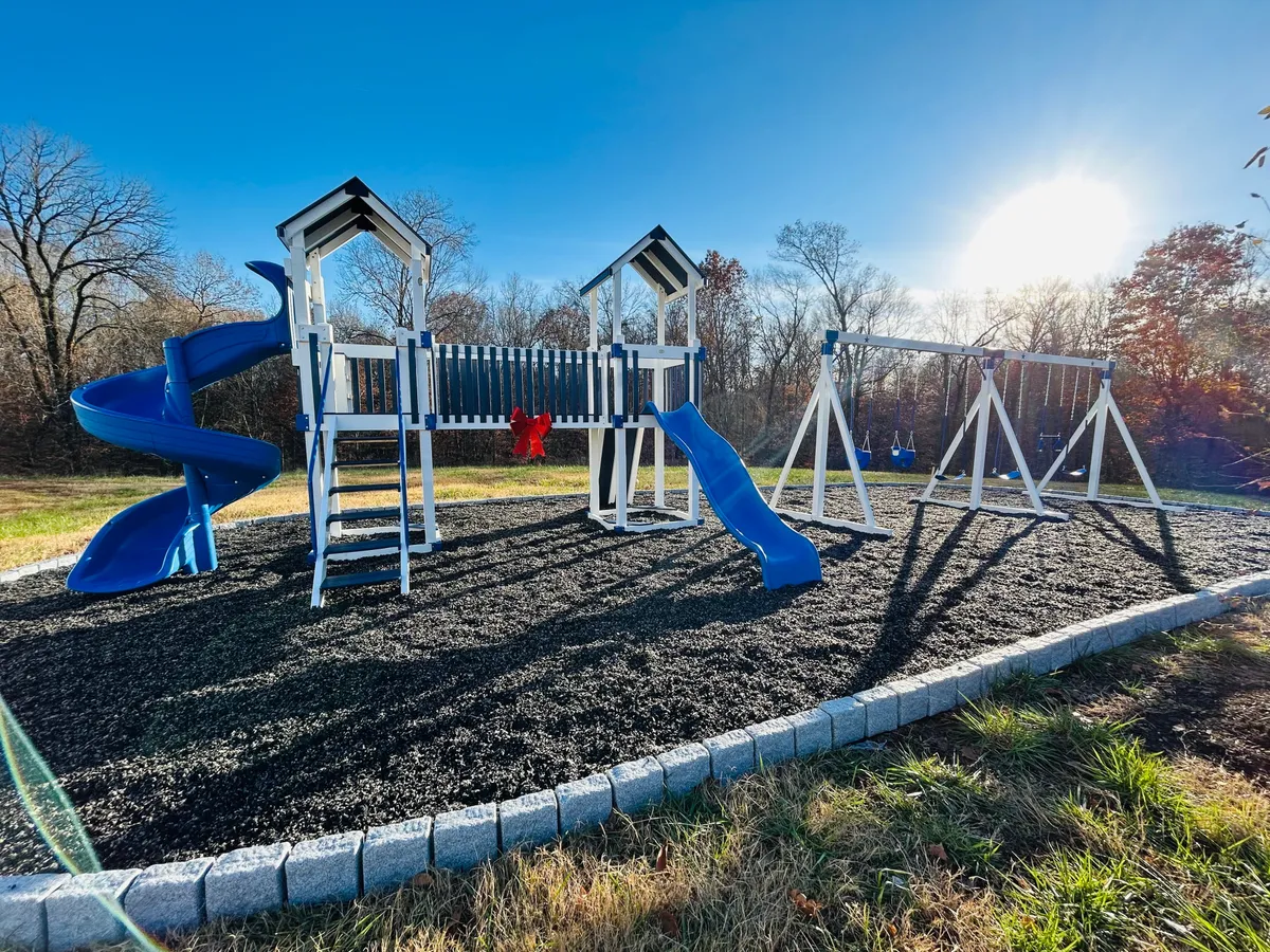 An inviting exterior scene featuring a vibrant playground with blue slides and a swing set, set in a park-like environment. The area is bustling with children at play, and the surroundings suggest ample green space for outdoor activities.