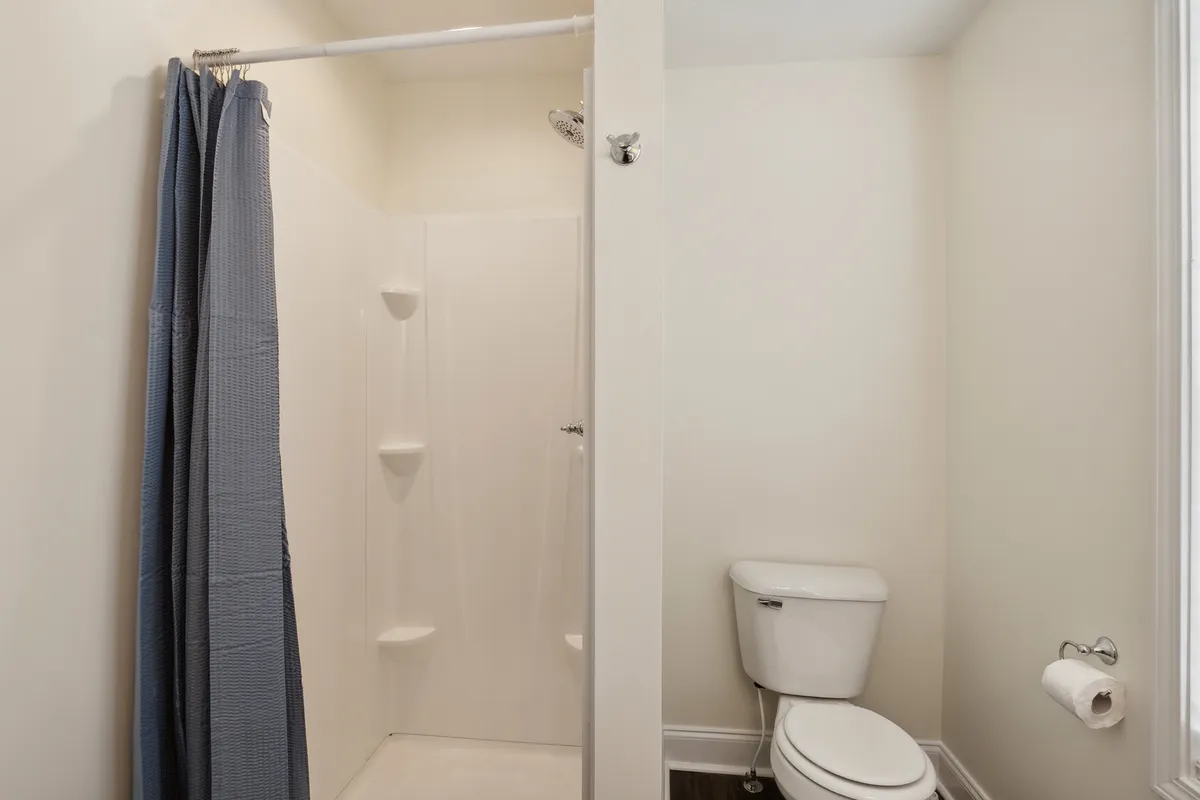 This image displays a modern bathroom featuring a pristine shower area, toilet, and a conveniently placed towel holder. The space is clean, calming, and designed for both relaxation and efficient routines.