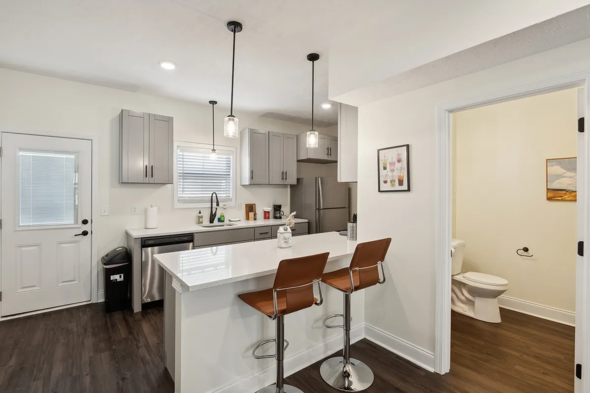 A bright, inviting kitchen with a central island, modern stainless steel appliances, and bar stools, illuminated by ample window light. The décor and layout encourage both cooking and socializing, while the open island provides a natural gathering spot.