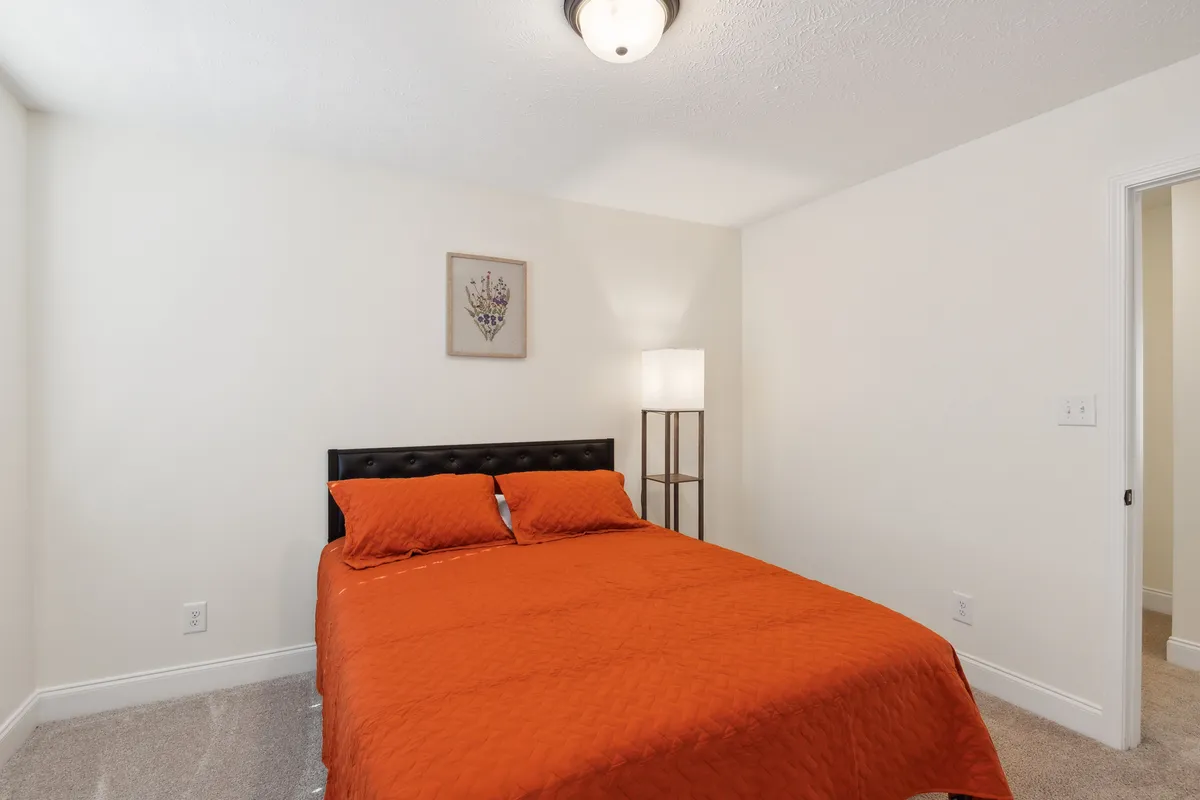 This image features a spacious bedroom with a bed adorned in orange bedding, complemented by decorative wall art and a cozy floor lamp. The space exudes comfort and tranquility, ideal for relaxation and restful sleep.