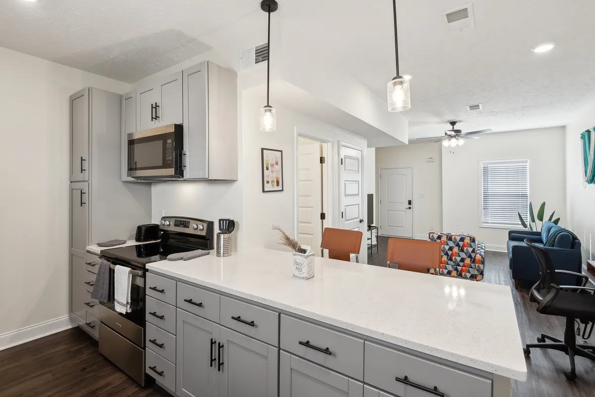A view of a stylish kitchen with a kitchen island, colorful chairs, and stainless steel appliances. Decorative artwork brings warmth, while the open layout connects seamlessly to the living space. The cheerful mood and thoughtful design details offer a sense of a well-prepared, move-in-ready home.